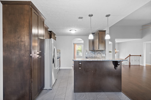 kitchen with light stone countertops, a textured ceiling, white refrigerator with ice dispenser, decorative light fixtures, and a breakfast bar