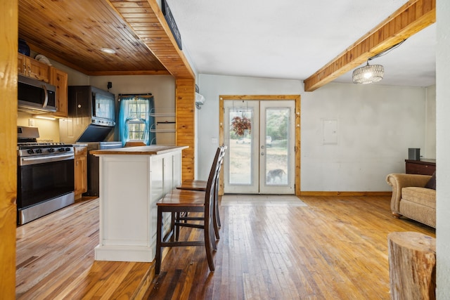 kitchen featuring french doors, a breakfast bar area, hanging light fixtures, appliances with stainless steel finishes, and light hardwood / wood-style floors