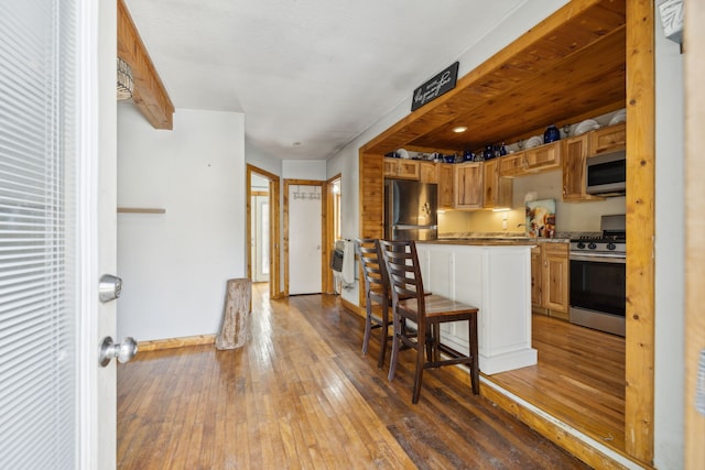 kitchen featuring hardwood / wood-style floors, appliances with stainless steel finishes, a kitchen bar, and heating unit