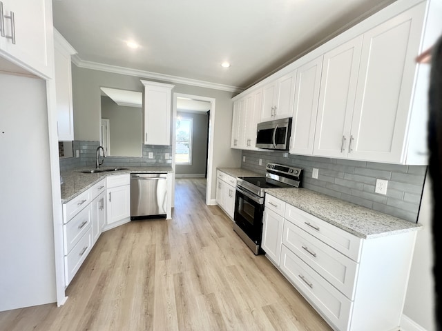 kitchen with appliances with stainless steel finishes, white cabinetry, light stone counters, and sink