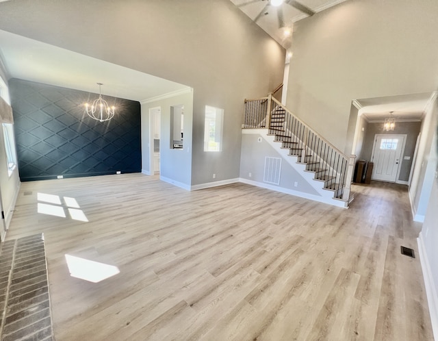 entryway with light wood-type flooring, a towering ceiling, an inviting chandelier, and ornamental molding