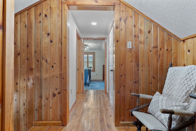 hall featuring lofted ceiling, light hardwood / wood-style flooring, ornamental molding, a textured ceiling, and wood walls