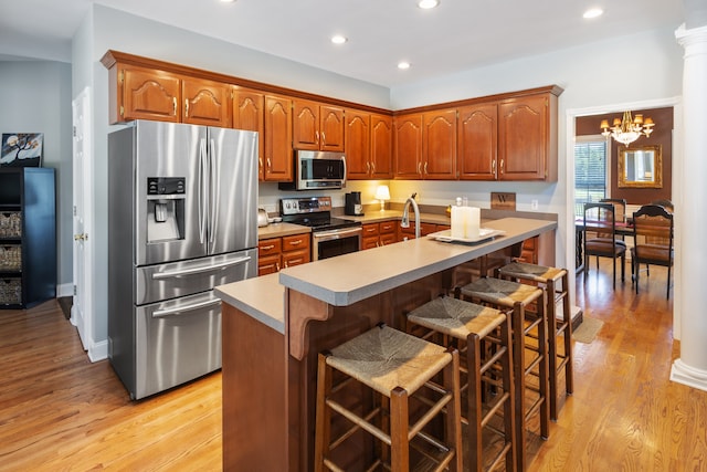 kitchen with a breakfast bar area, appliances with stainless steel finishes, light wood-type flooring, and an island with sink