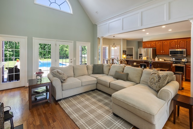 living room featuring decorative columns, a notable chandelier, high vaulted ceiling, and wood-type flooring