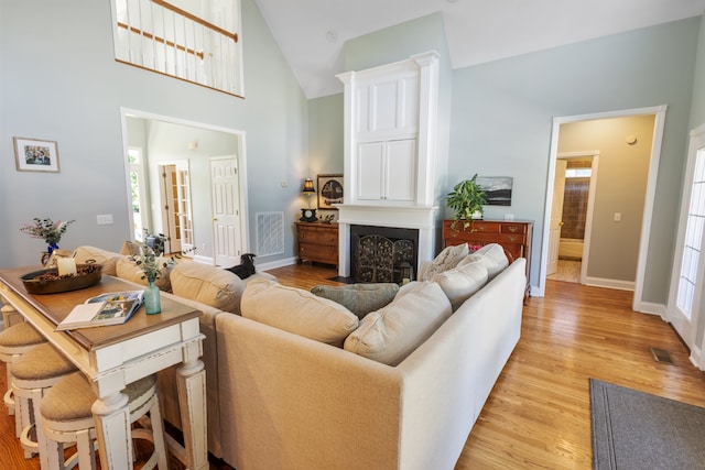 living room featuring high vaulted ceiling, light wood-type flooring, and a fireplace