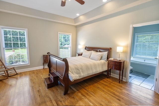 bedroom featuring light hardwood / wood-style floors, multiple windows, ensuite bath, and ceiling fan