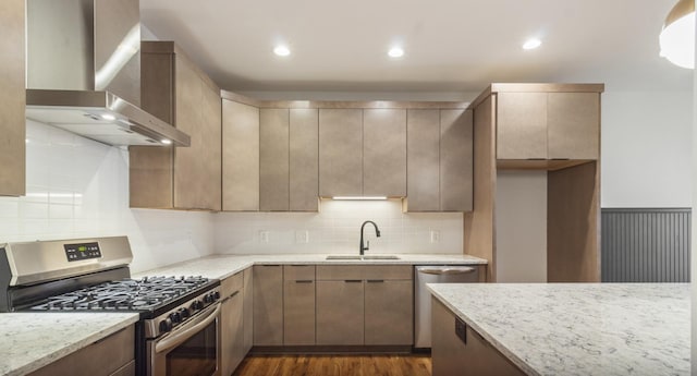 kitchen with appliances with stainless steel finishes, wall chimney range hood, dark hardwood / wood-style floors, light stone countertops, and sink