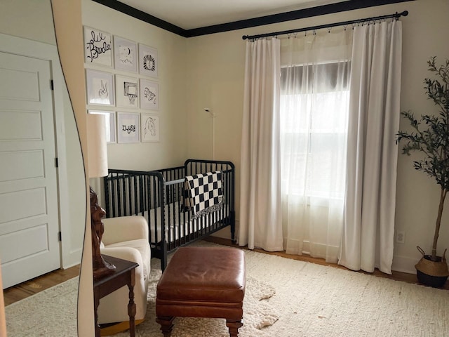 bedroom with a crib, ornamental molding, and hardwood / wood-style floors