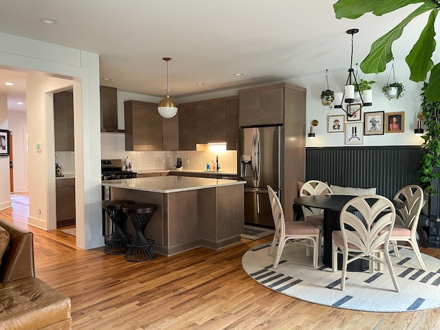 kitchen with light hardwood / wood-style floors, appliances with stainless steel finishes, dark brown cabinets, hanging light fixtures, and sink