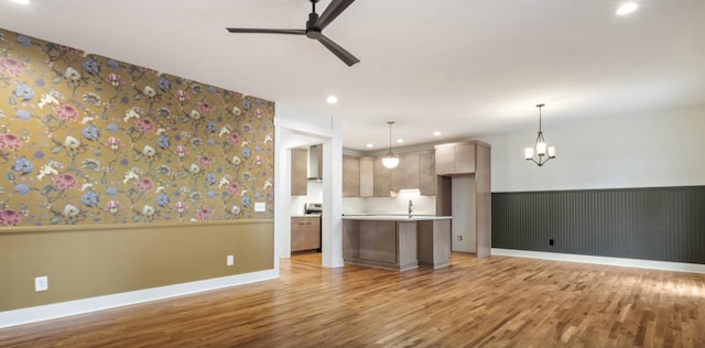 unfurnished living room featuring sink, ceiling fan with notable chandelier, and light hardwood / wood-style flooring