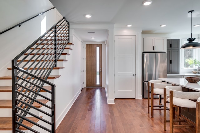 kitchen featuring white cabinets, wood-type flooring, decorative light fixtures, and stainless steel fridge