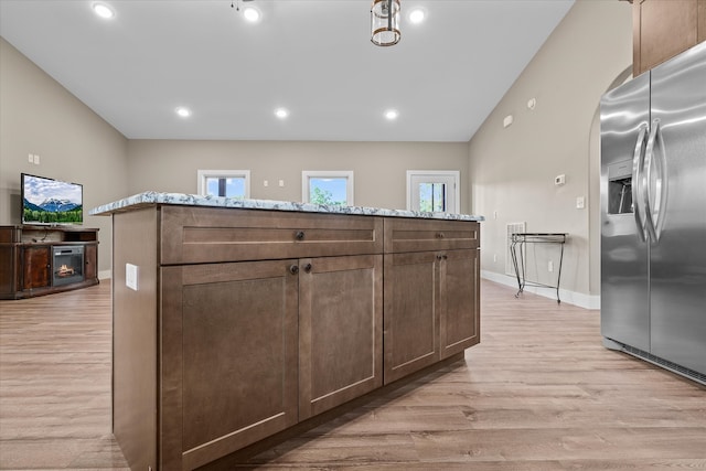 kitchen featuring stainless steel fridge, light stone counters, vaulted ceiling, light hardwood / wood-style flooring, and a center island