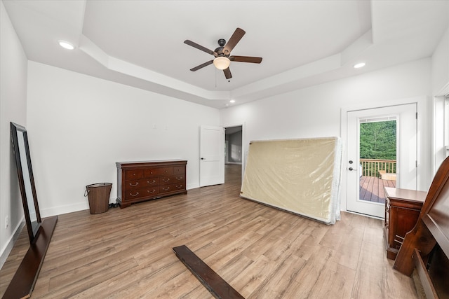 unfurnished bedroom featuring light hardwood / wood-style floors, access to outside, ceiling fan, and a raised ceiling