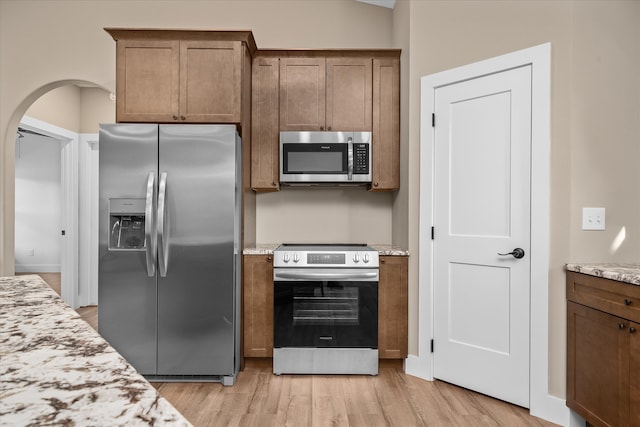 kitchen featuring appliances with stainless steel finishes, light hardwood / wood-style flooring, and light stone counters