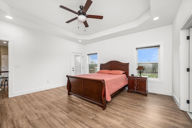 bedroom featuring a tray ceiling, baseboards, and light wood finished floors