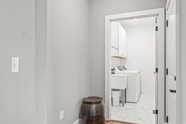 bathroom featuring baseboards, washing machine and dryer, marble finish floor, and a sink