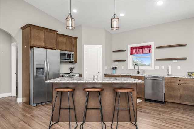 kitchen featuring a kitchen island, open shelves, arched walkways, stainless steel appliances, and light wood-style floors