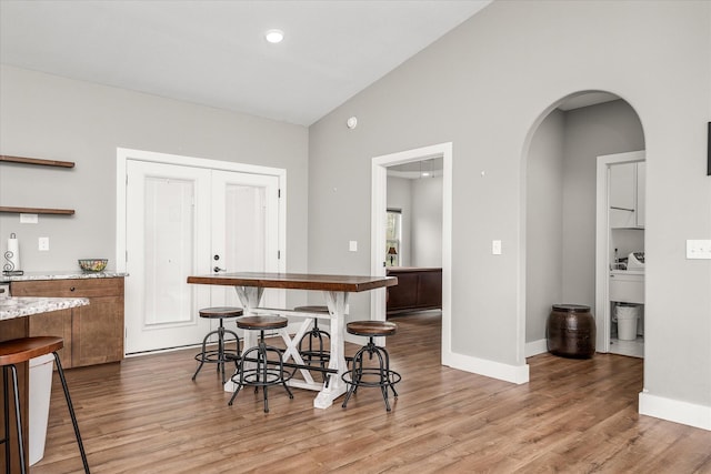 kitchen with a kitchen bar, open shelves, arched walkways, light wood-style floors, and baseboards