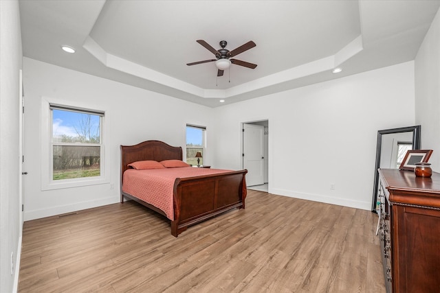 bedroom featuring light wood finished floors, multiple windows, a raised ceiling, and baseboards