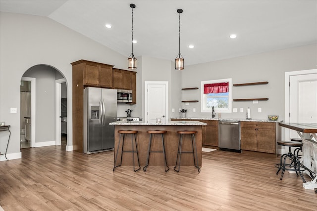 kitchen with light wood finished floors, a kitchen island, arched walkways, stainless steel appliances, and open shelves