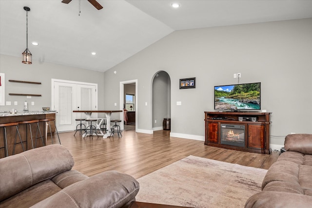 living area featuring baseboards, lofted ceiling, wood finished floors, arched walkways, and a ceiling fan