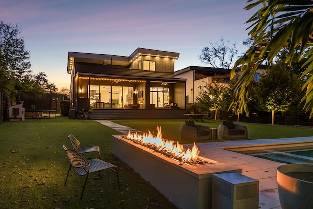 back house at dusk with a yard, an outdoor fire pit, a trampoline, and a patio