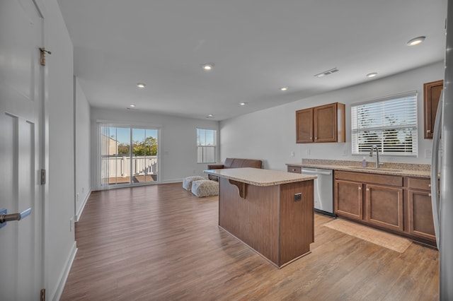 kitchen with sink, light hardwood / wood-style flooring, dishwasher, a kitchen island, and a breakfast bar area