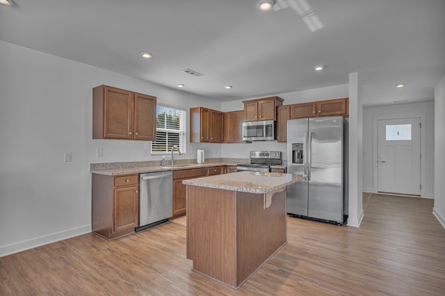 kitchen with light wood-type flooring, stainless steel appliances, a kitchen island, and sink