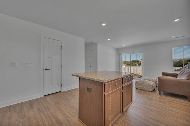 kitchen with a kitchen island, light stone countertops, and light hardwood / wood-style floors