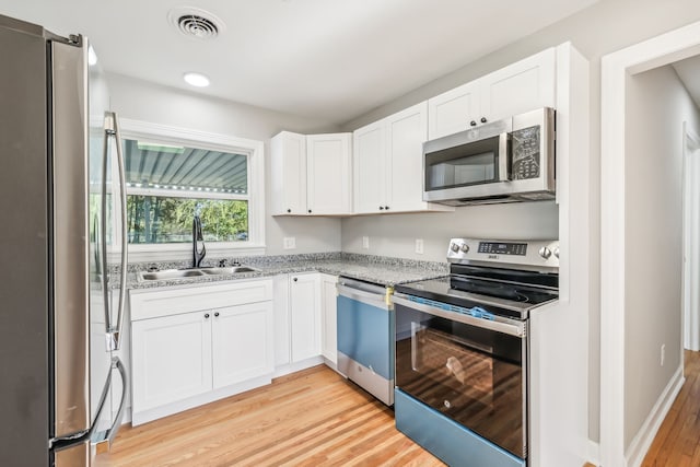 kitchen featuring sink, light stone countertops, white cabinets, appliances with stainless steel finishes, and light hardwood / wood-style floors