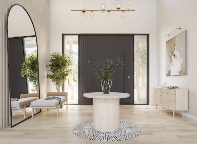 entryway featuring light wood-type flooring, a towering ceiling, and a chandelier