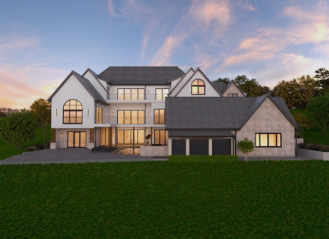 back house at dusk with a balcony, a patio area, and a lawn