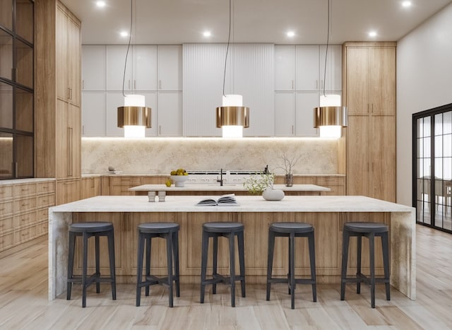 kitchen featuring a kitchen bar, a center island with sink, white cabinets, and pendant lighting