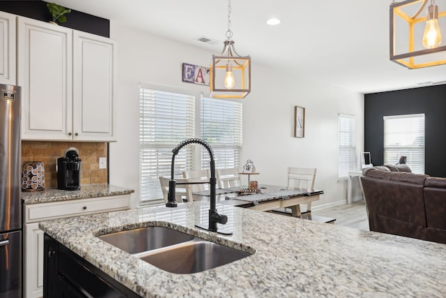 kitchen with tasteful backsplash, sink, white cabinetry, decorative light fixtures, and light stone counters