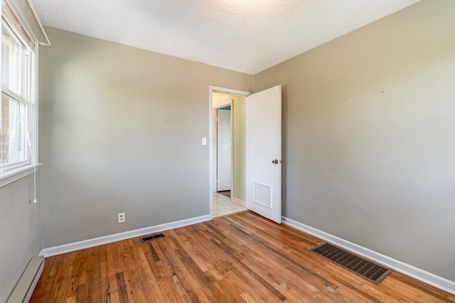 empty room with a baseboard radiator, light hardwood / wood-style flooring, and plenty of natural light