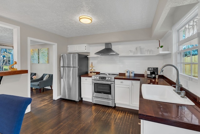 kitchen featuring wall chimney range hood, appliances with stainless steel finishes, dark hardwood / wood-style flooring, a wealth of natural light, and white cabinets