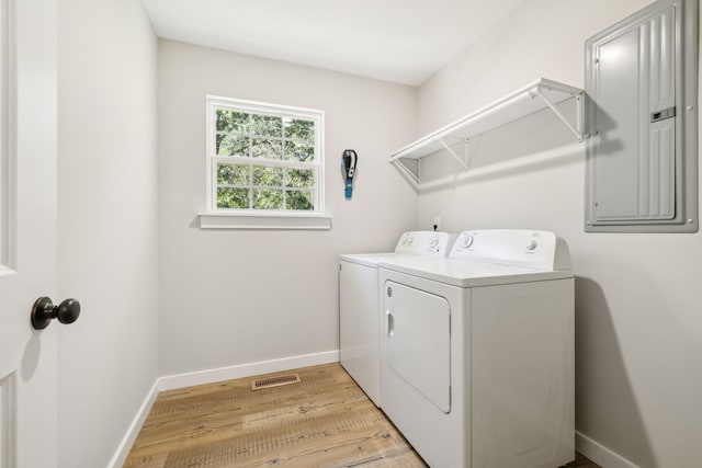 clothes washing area with light wood-type flooring, electric panel, and separate washer and dryer