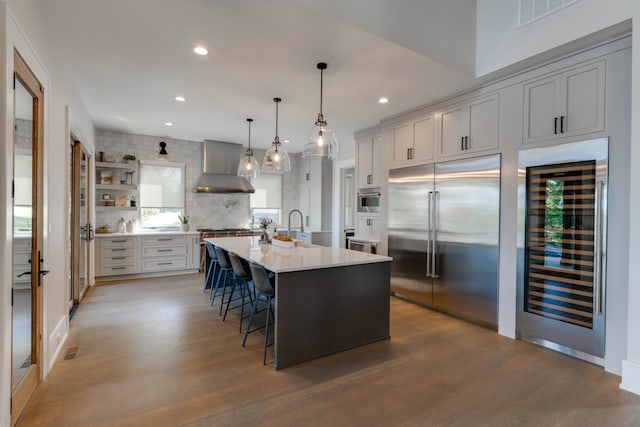 kitchen with wall chimney range hood, wine cooler, a breakfast bar area, appliances with stainless steel finishes, and a spacious island