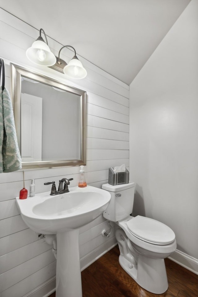 bathroom featuring toilet, hardwood / wood-style floors, wooden walls, and vaulted ceiling