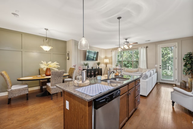 kitchen featuring wood-type flooring, sink, hanging light fixtures, stainless steel dishwasher, and a center island with sink