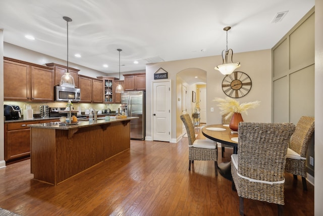 kitchen featuring hanging light fixtures, a kitchen breakfast bar, a kitchen island with sink, dark hardwood / wood-style floors, and stainless steel appliances