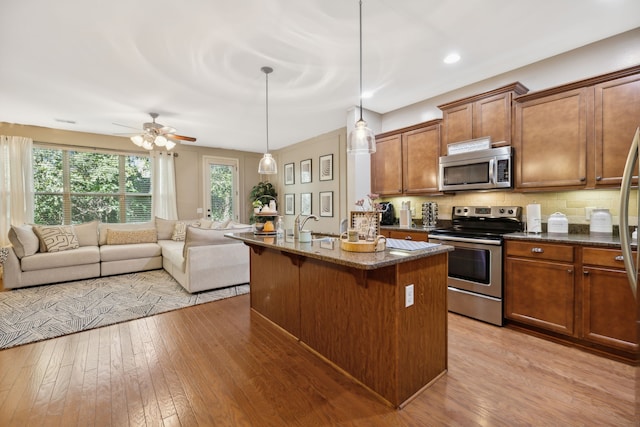 kitchen featuring appliances with stainless steel finishes, a kitchen breakfast bar, decorative light fixtures, light hardwood / wood-style flooring, and a center island with sink