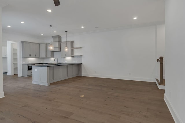 kitchen with crown molding, open shelves, a sink, wood finished floors, and a peninsula