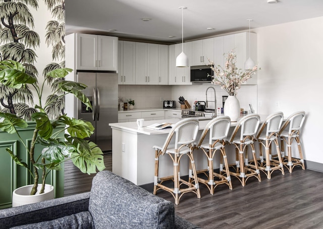 kitchen with dark wood-type flooring, hanging light fixtures, white cabinets, appliances with stainless steel finishes, and tasteful backsplash