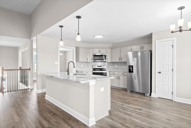 kitchen with light stone countertops, appliances with stainless steel finishes, sink, and pendant lighting