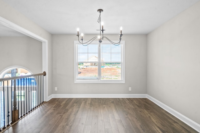 spare room featuring dark wood-type flooring, a notable chandelier, and a healthy amount of sunlight