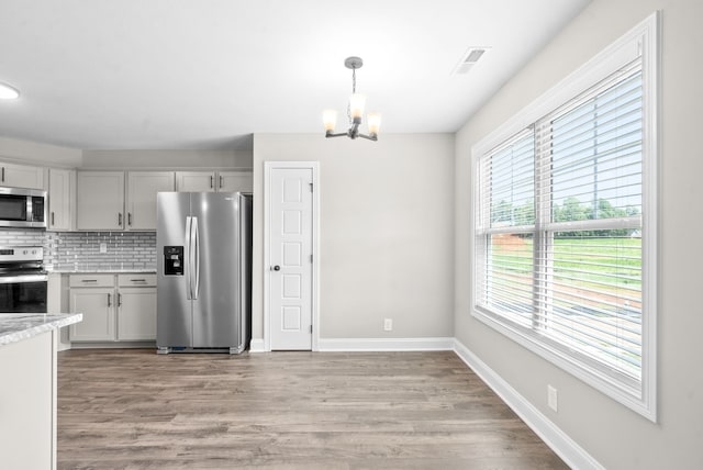 kitchen with decorative light fixtures, tasteful backsplash, a notable chandelier, light hardwood / wood-style flooring, and stainless steel appliances