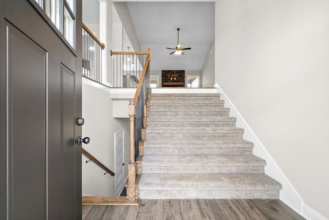 stairs with ceiling fan, a high ceiling, and hardwood / wood-style flooring