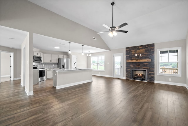 unfurnished living room featuring a wealth of natural light, dark hardwood / wood-style flooring, and a stone fireplace