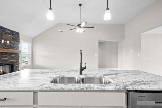 kitchen featuring white cabinetry, lofted ceiling, a stone fireplace, and sink